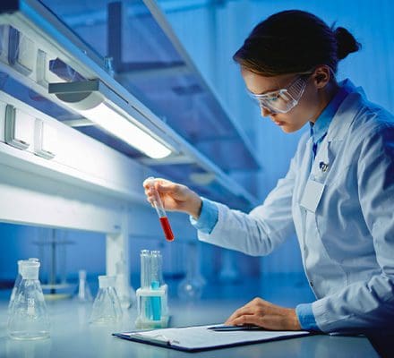 Woman views test tube at lab station.