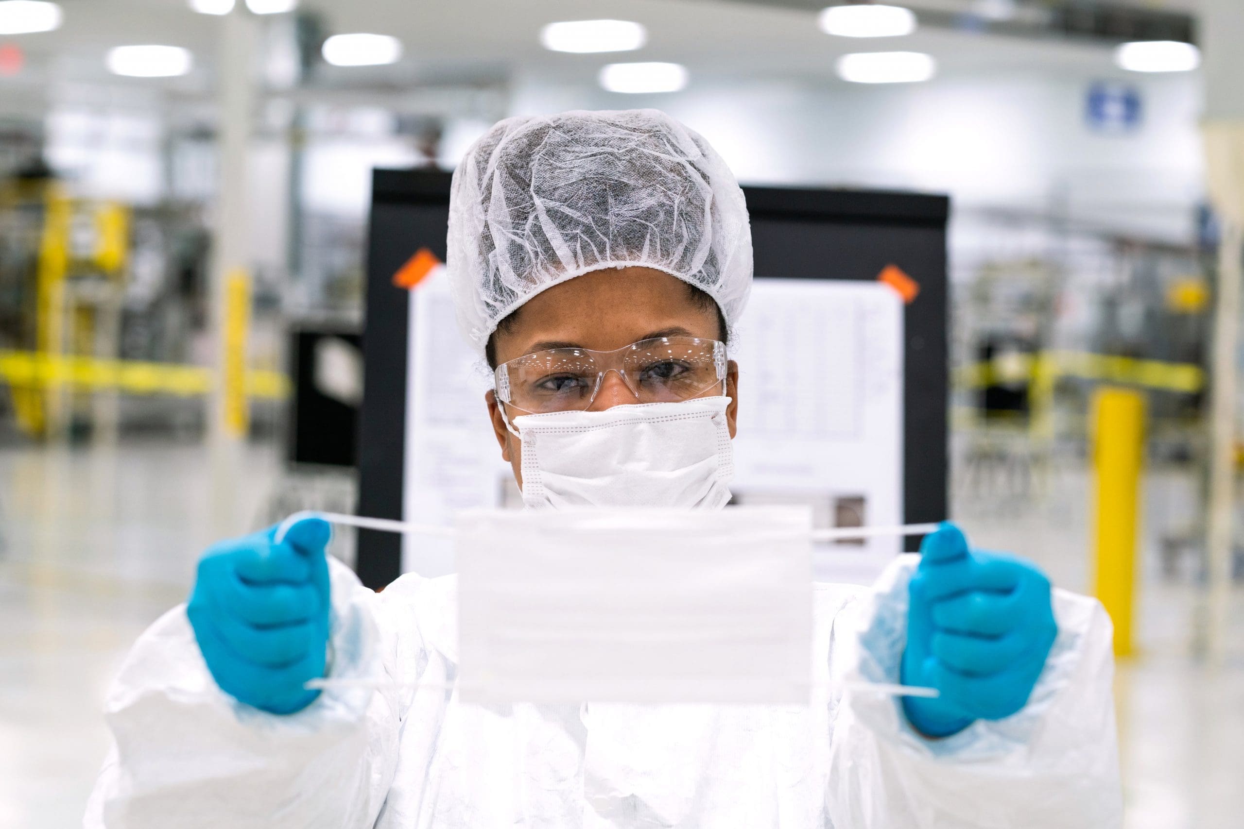 Worker in protective gear stretches face mask at eye level.